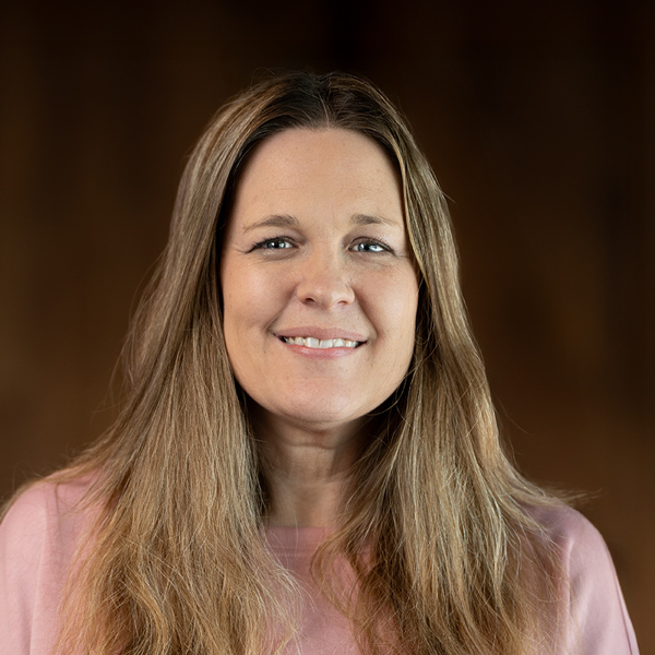 Kari Havens, Resident Services Director at Curtis Creek Senior Living, smiling gently while wearing a pink top, with long blonde hair against a softly lit background.