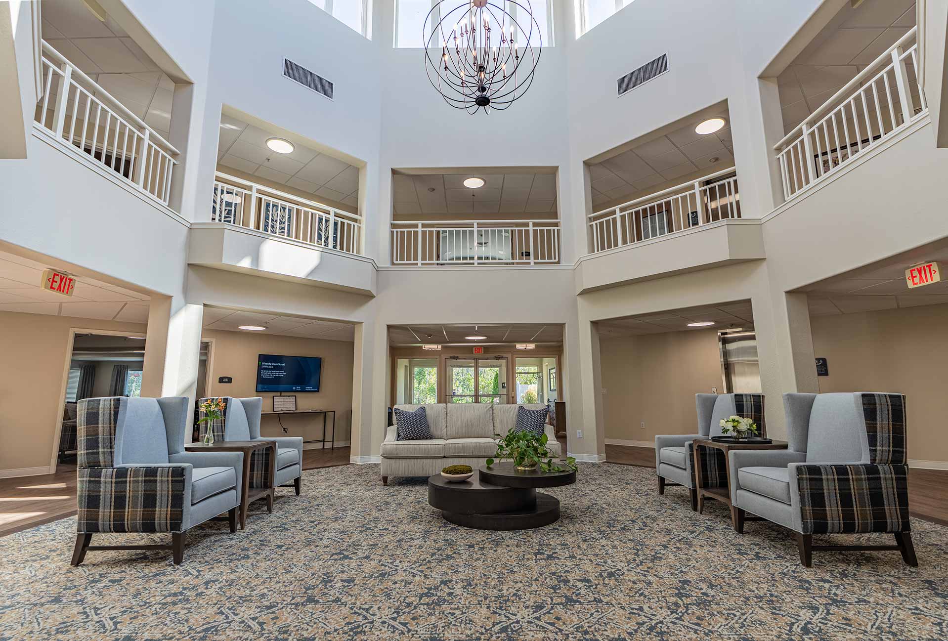 A bright and elegant senior living lobby with high ceilings, comfortable seating, a patterned rug, and natural light creating a welcoming and sophisticated atmosphere.