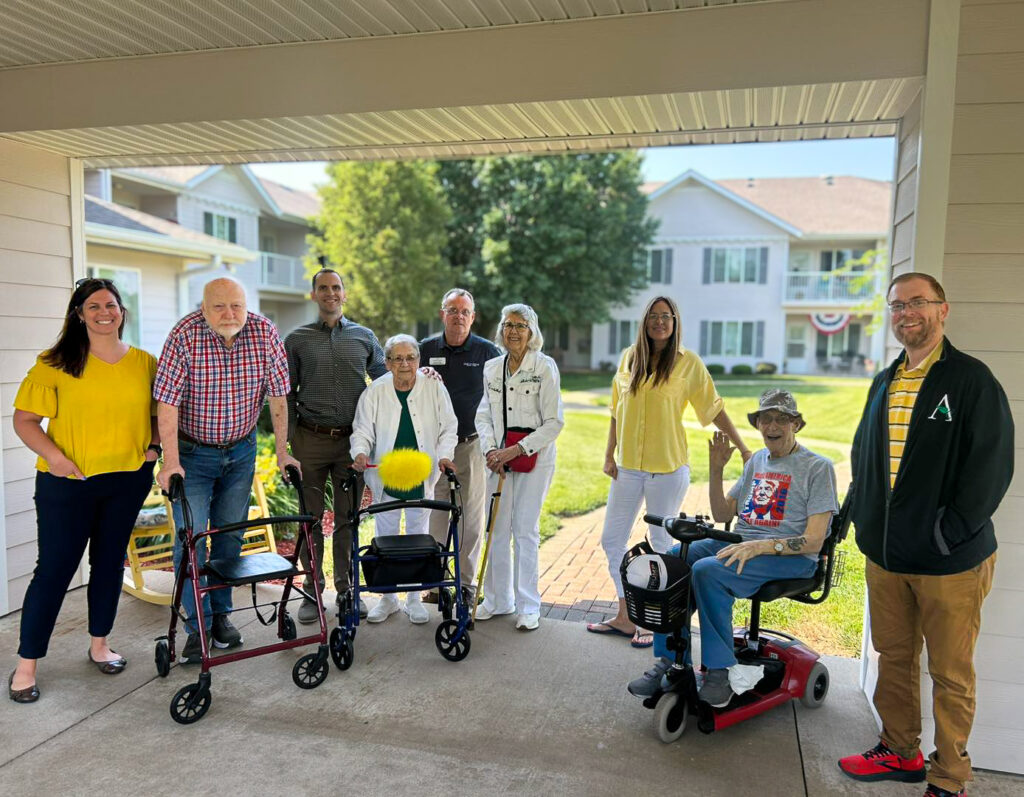 Residents and team members smile for a group photo outdoors during a sunny day.