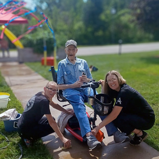 Two team members and a senior man enjoy a Summer event outdoors.