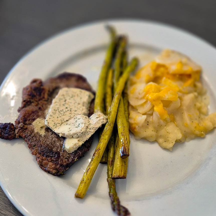 A plate full of chef-prepared steak with herb butter, roasted asparagus, and scallop potatoes.