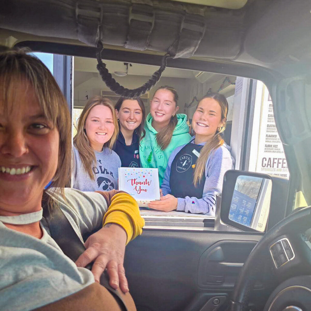 A Curtis Creek Senior Living team member smiles from her car, presenting a card to four women from a local drive-through business.